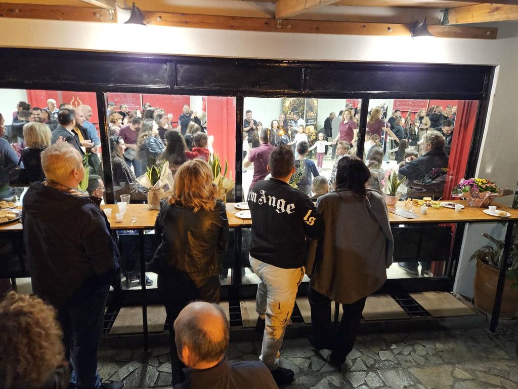 Επισκέπτες στο μπαρ της αυλής κοιτούν τη γεμάτη αίθουσα του συλλόγου τη βραδιά των εγκαινίων
