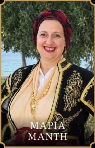 Φωτογραφία της Μαρίας Μαντή με παραδοσιακή Κρητική φορεσιά. Φοράει μαύρο γιλέκο με χρυσά κεντήματα, μπεζ πουκάμισο, κόκκινο μαντήλι στα μαλλιά, χρυσό κρεμαστό κόσμημα με αλυσίδα στο λαιμό και κόκκινο ζωνάρι στη μέση.